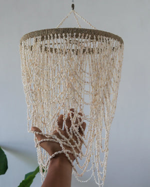 Hand touching a white beaded seashell chandelier with cascading strands, boho home decor