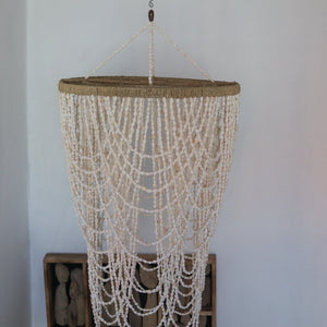 Handmade Balinese seashell chandelier with cascading white bead strands against white wall