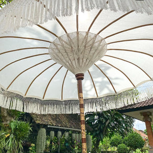 White Balinese parasol with decorative fringe in a tropical garden setting