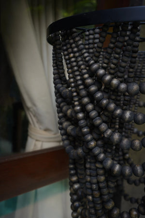Close-up of black wooden beads on a boho chandelier, with curtain background