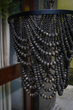 Handmade beaded chandelier with dark wooden beads, hanging outdoors by a window