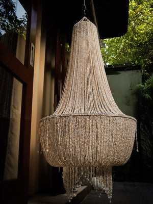 Handmade seashell chandelier hanging outdoors, featuring intricate beadwork and natural light