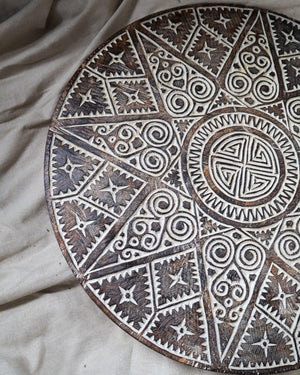 Hand-carved round wooden decor panel with intricate tribal geometric patterns
