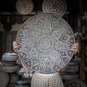 Hand holding large round Balinese carved wooden wall art with intricate tribal patterns