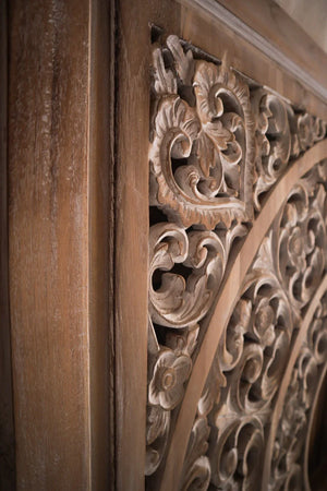 Hand-carved Balinese wood door detail with intricate floral and scrollwork patterns.