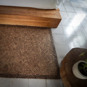 Handwoven natural fiber rug on tile floor beside wooden bed and rustic table in bedroom