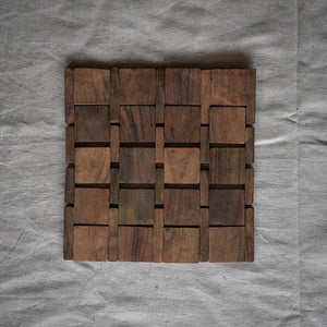 Handmade teak wood trivet with geometric pattern on neutral fabric background