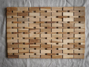 Handmade rectangular wooden bath mat with woven slat pattern on neutral fabric background