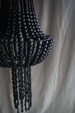 Black beaded chandelier with cascading strands against a neutral fabric backdrop